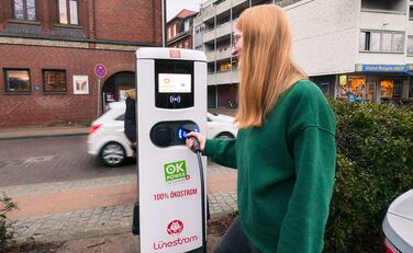 Frau steckt den Stecker eines E-Autos in eine Lünestrom-Ladesäule