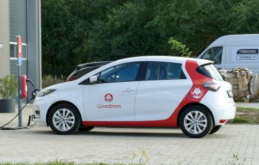 Weißes Auto mit rotem Lünestrom-Branding wird an einer Ladesäule geladen.