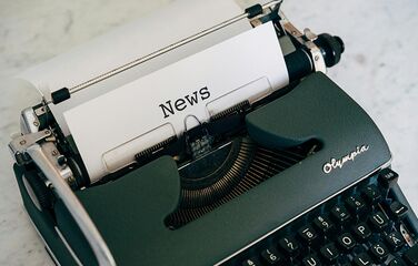 Schreibmaschine mit einem eingespannten Blatt auf dem News steht.