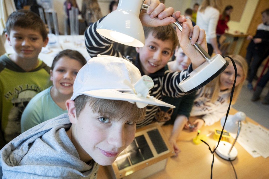Mit einer Lampe treibt ein Schüler den solarbetriebenen Ventilator an der Cap eines Mitschülers an.